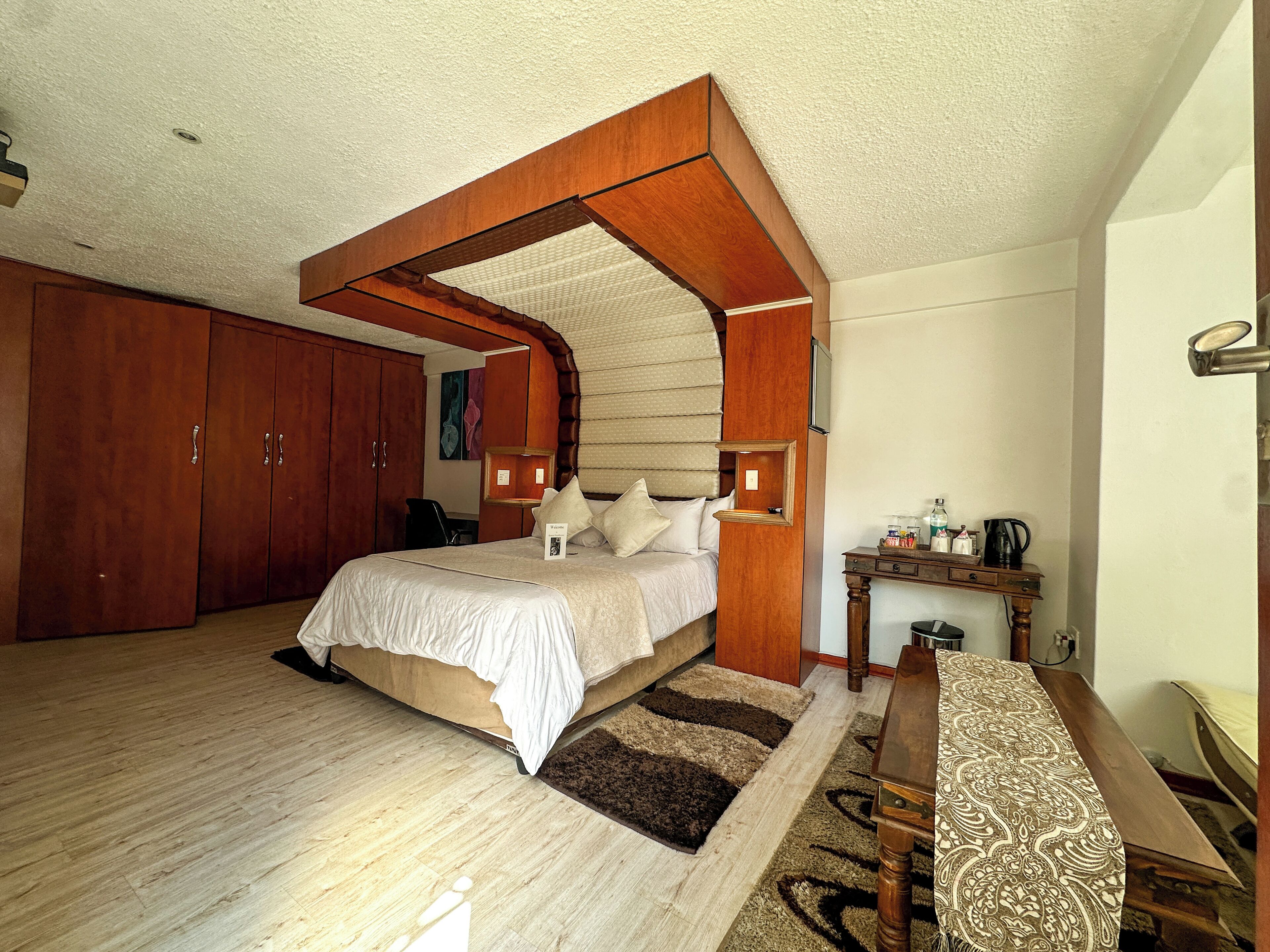 A bedroom with a wooden canopy bed, a desk with a chair, a nightstand, and a large wardrobe.