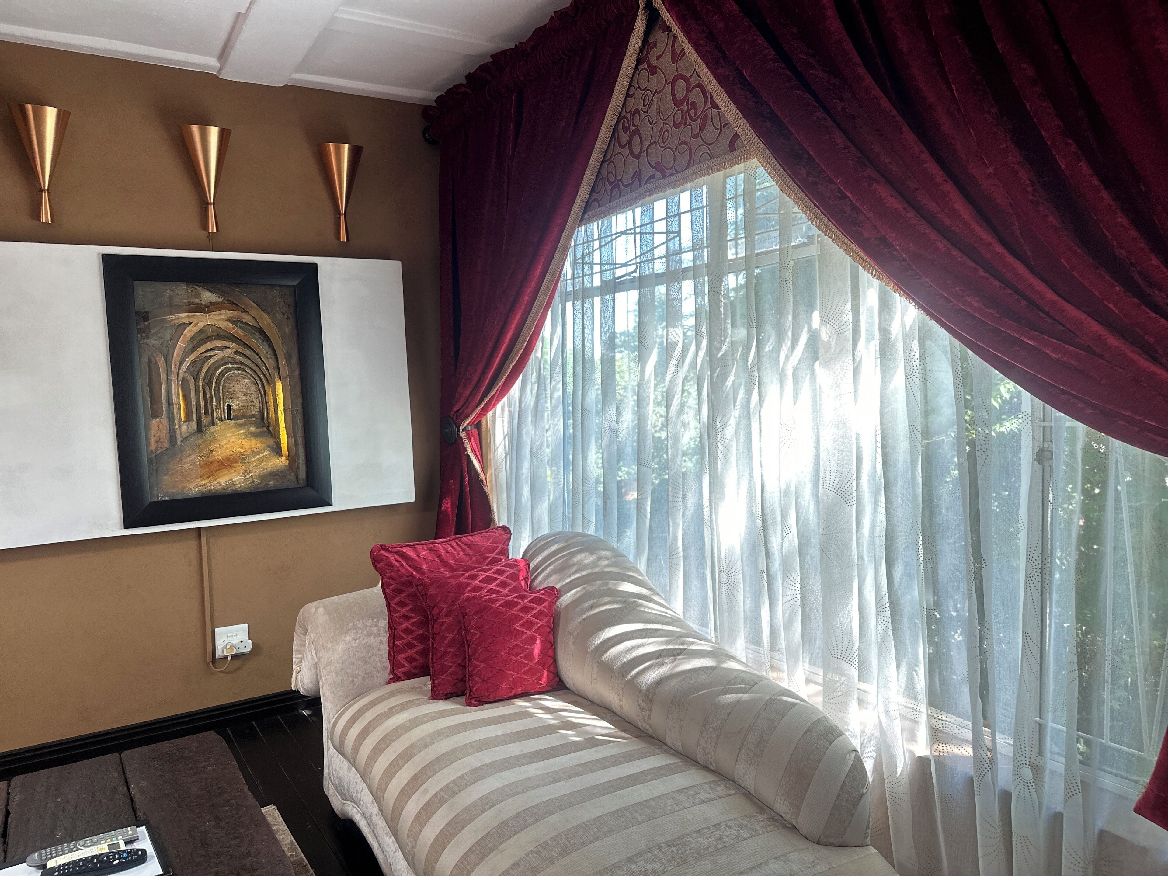 A bedroom with a bed, a painting, a window with curtains, and wall sconces.