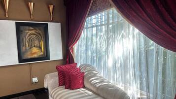 A bedroom with a bed, a painting, a window with curtains, and wall sconces.
