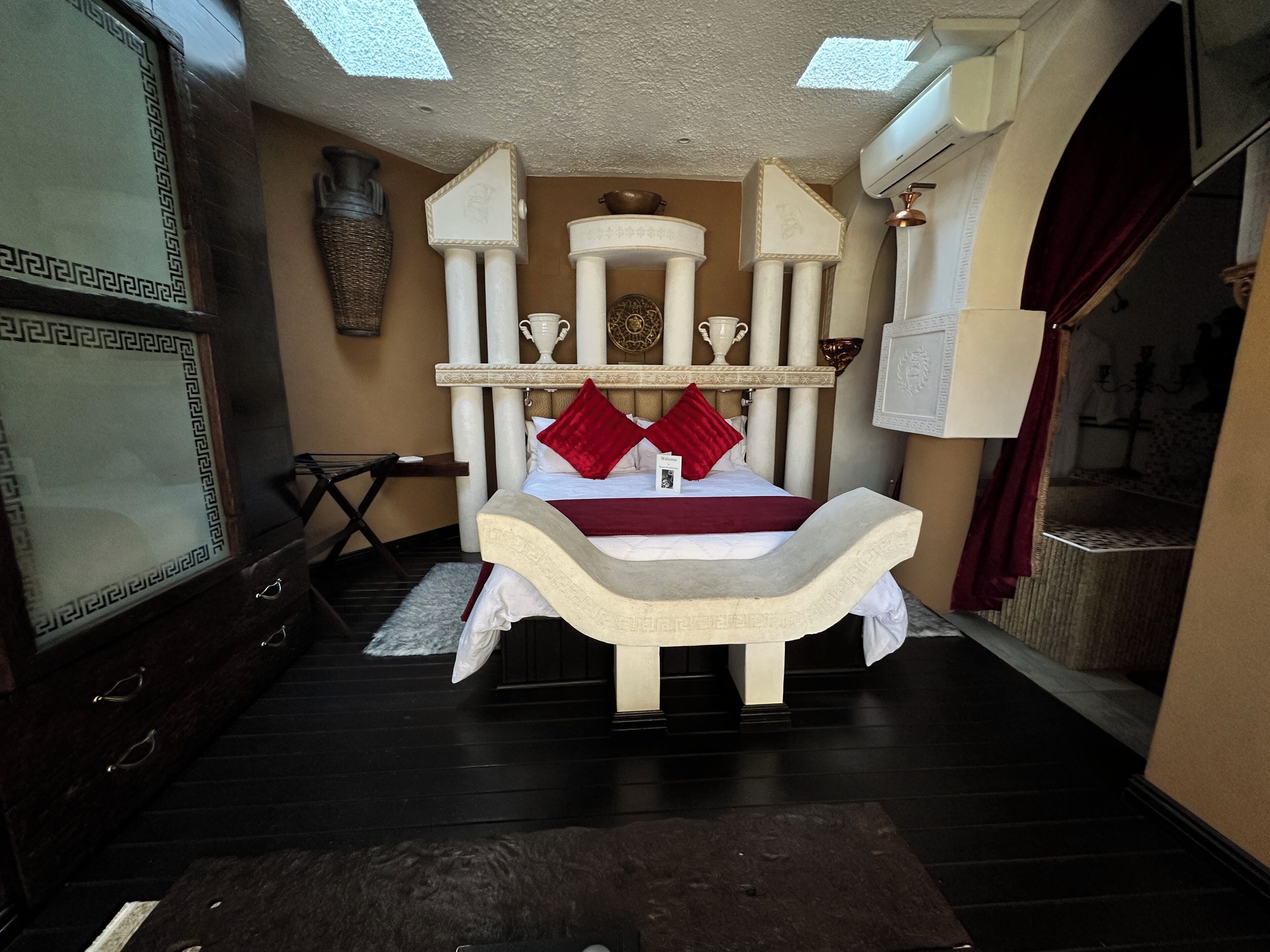A room with a bed, a desk, a chair, and a large vase on the wall.