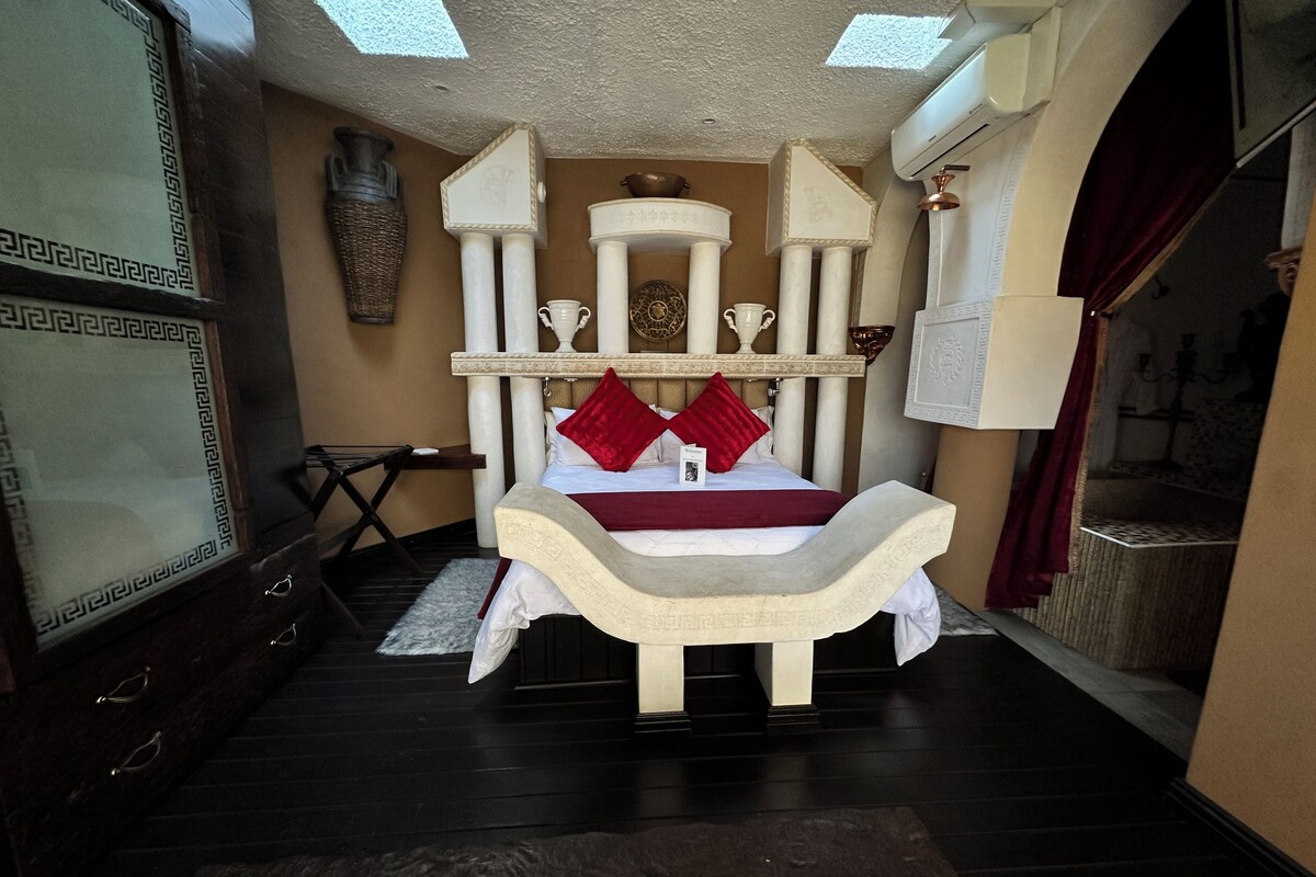 Een kamer met een bed, een bureau, een stoel en een grote vaas aan de muur.