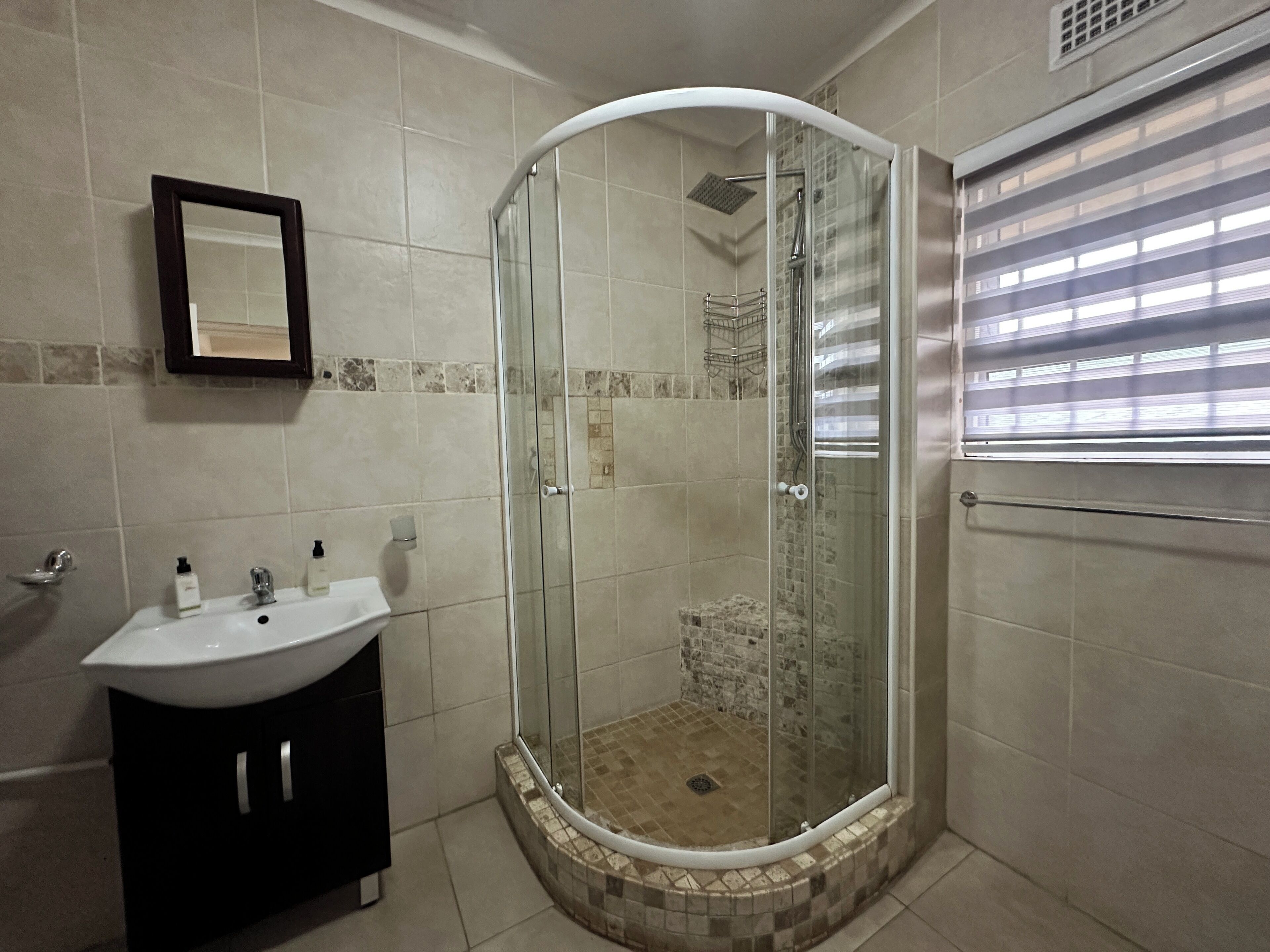 Un baño con ducha envuelta en vidrio, un lavamanos y un espejo.