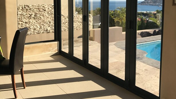 A room with large sliding glass doors leading to a pool area, a chair, and a floor mat with text. - 11 Escape Views (Cape Town)