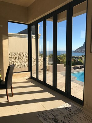 A room with large sliding glass doors leading to a pool area, a chair, and a floor mat with text. - 11 Escape Views (Cape Town)