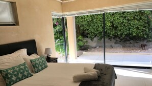 A hotel room with a large bed, a nightstand with a lamp, and a view of a garden through a sliding glass door. - 11 Escape Views (Cape Town)