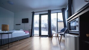 A modern bedroom with a bed, a desk, a chair, a television, and a view of mountains through the window. - Hótel Hafnarfjall (Hvalfjarðarsveit)