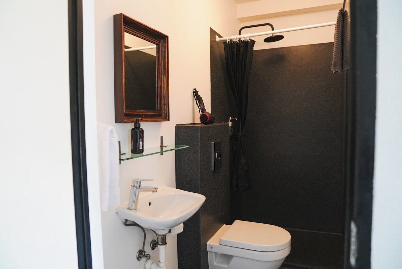 A compact bathroom with a white sink, a mirror, a toilet, and a shower area.