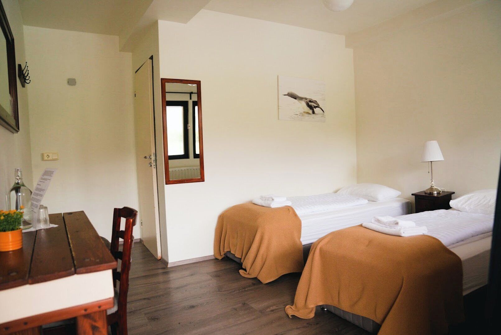 A hotel room with two beds, a wooden desk, a chair, a table with a plant, a mirror, and a lamp.