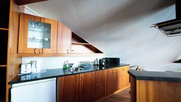 A kitchen with wooden cabinets, a black countertop, a microwave, and a small refrigerator.