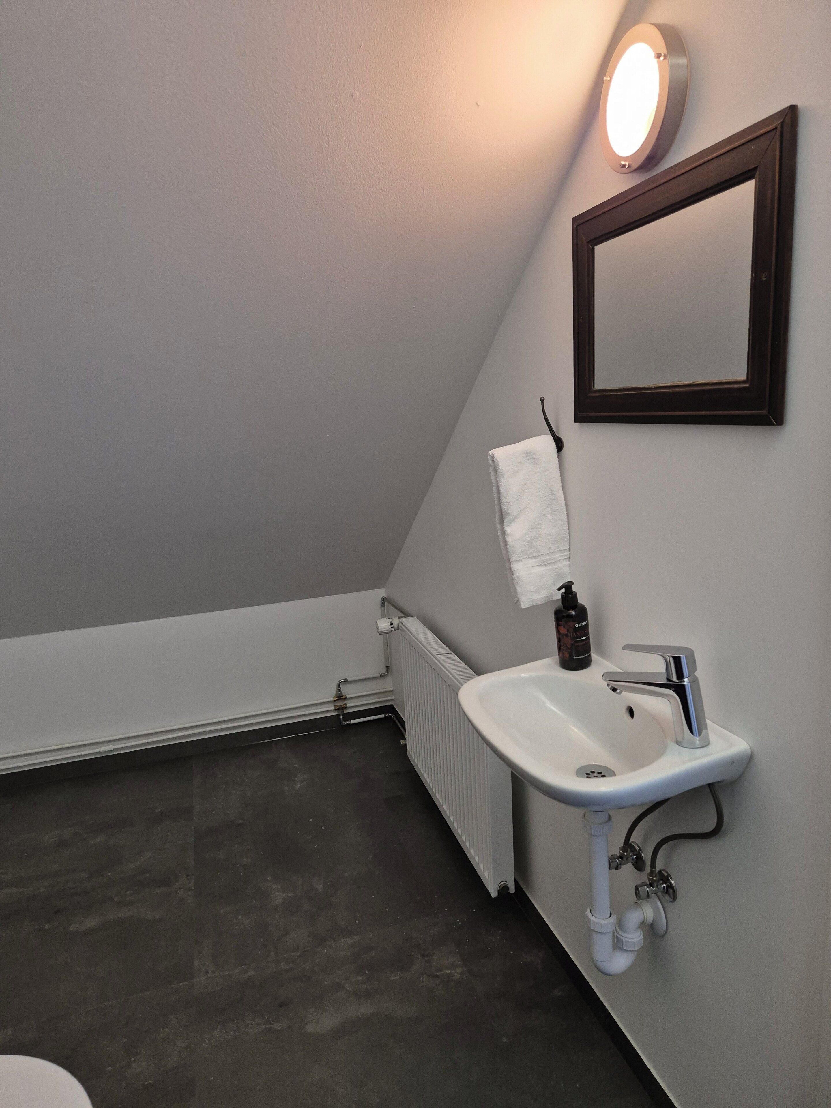 Een badkamer met een witte wastafel, een spiegel en een handdoek aan de muur.