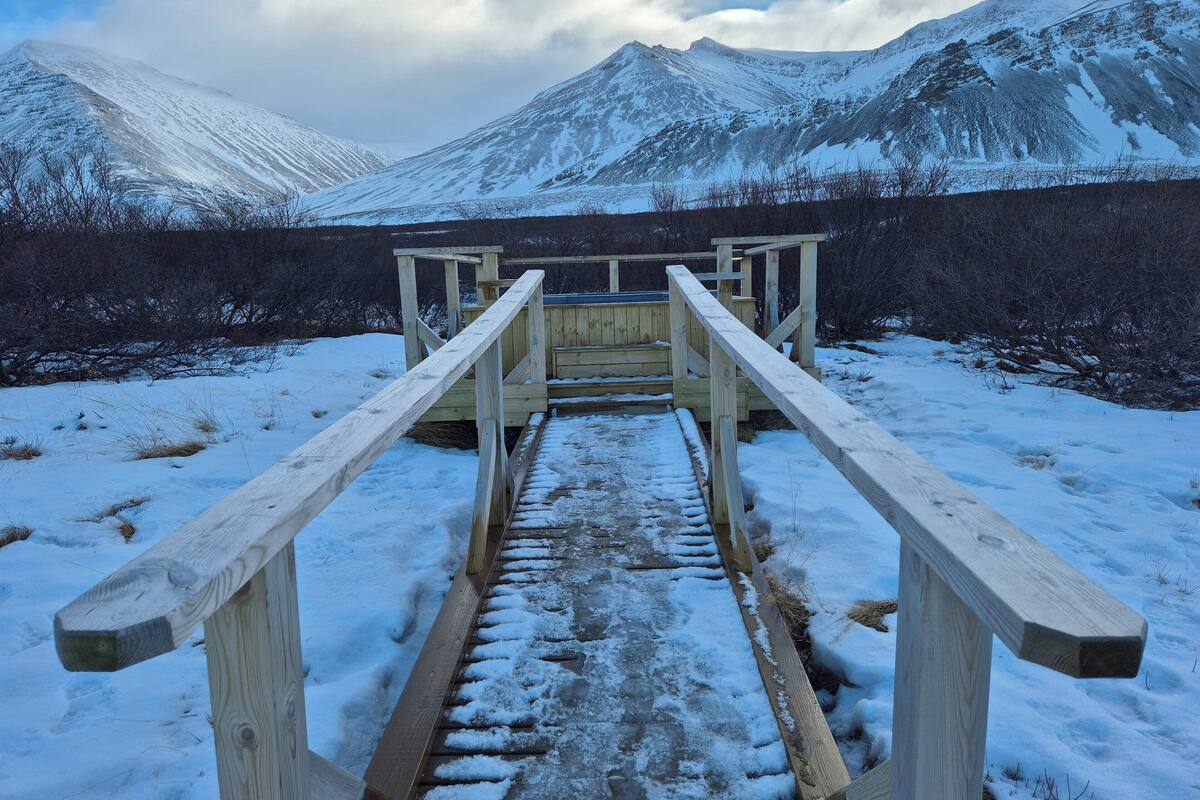 A wooden staircase leading to a wooden platform with a view of snow-covered mountains.