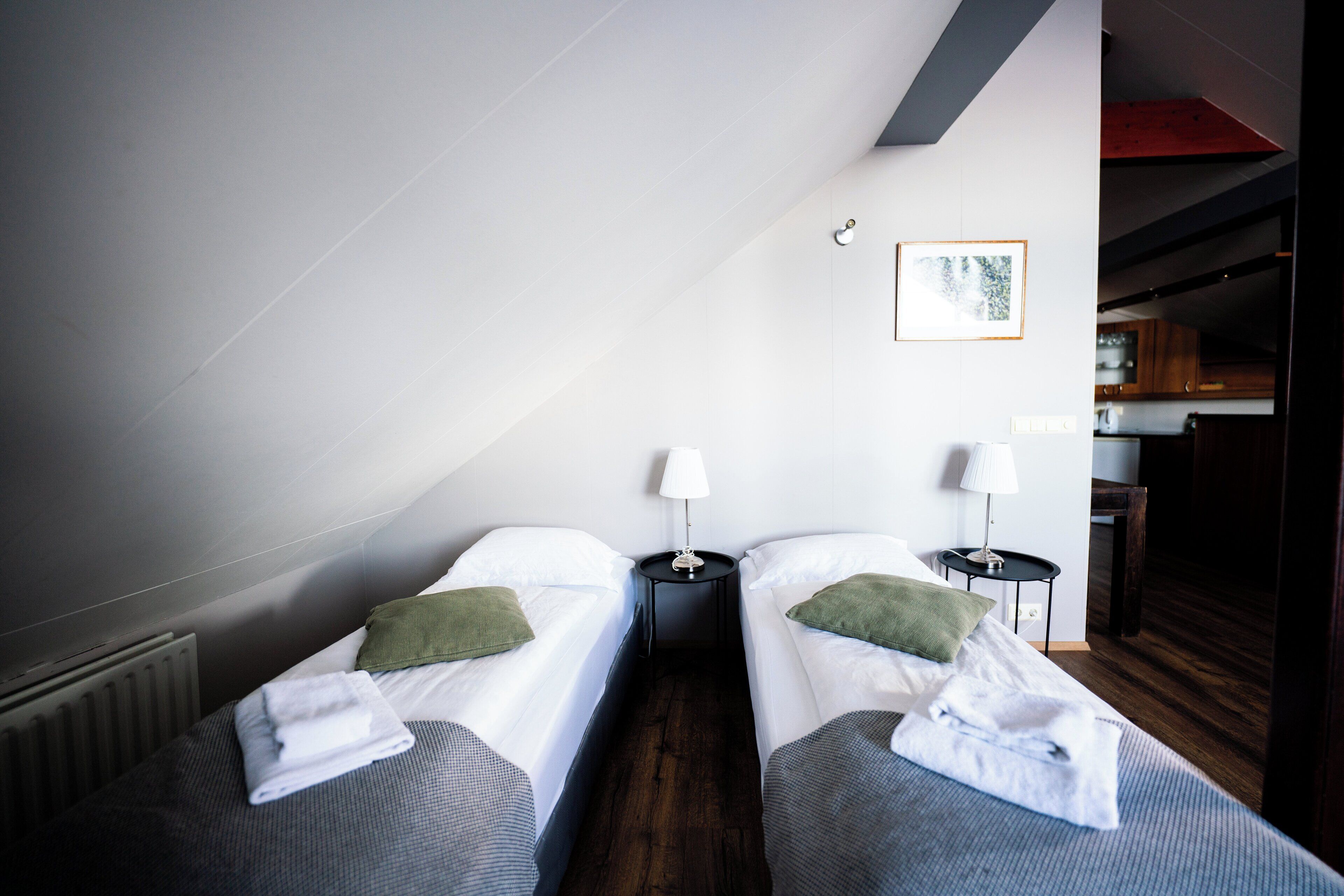 Quarto de hotel com duas camas, cada uma com um travesseiro e uma toalha enrolada. Há duas mesas de cabeceira com abajures.