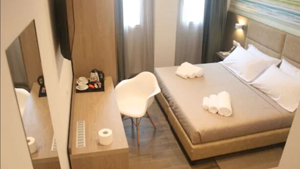 Habitación de hotel con una cama, un escritorio con una silla, un televisor y una ventana con cortinas.