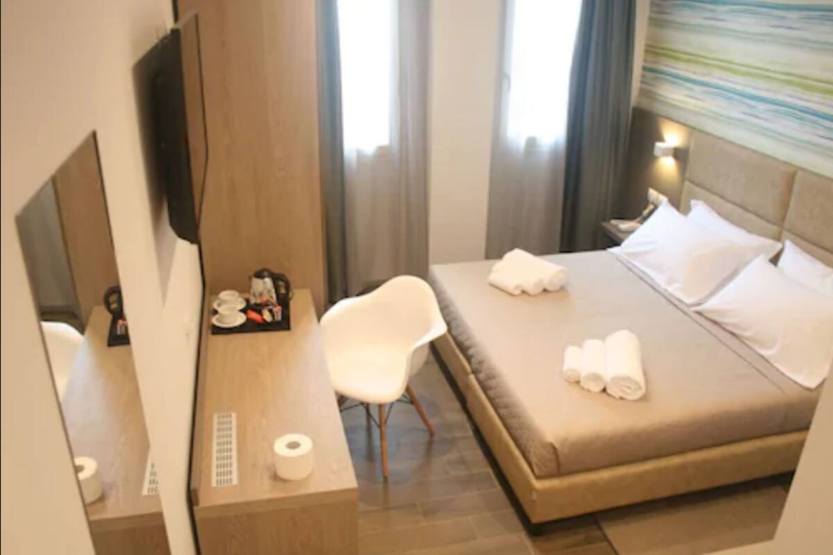 A hotel room with a bed, a desk with a chair, a TV, and a window with curtains.