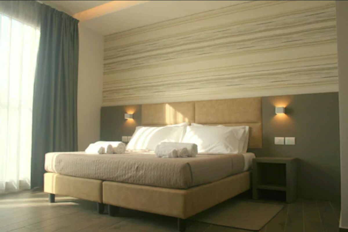 A modern bedroom with a large bed, two bedside tables, and a headboard with integrated lighting.