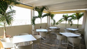 Un restaurante con terraza, mesas y sillas blancas, y plantas en macetas.