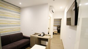 Un espacio habitable compacto con sofá, una mesita, kitchenette y un espejo.