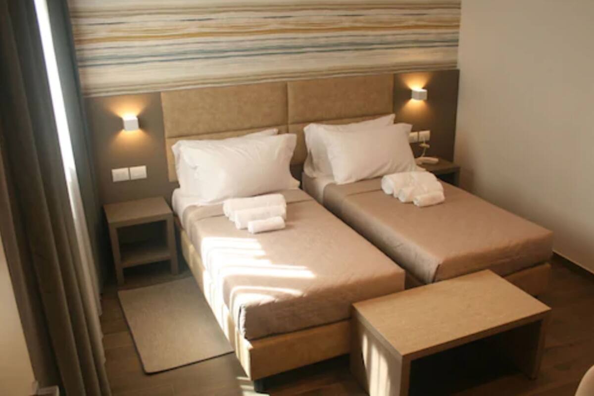 A hotel room with two beds, a small bedside table, a nightstand, and a foldable bench.
