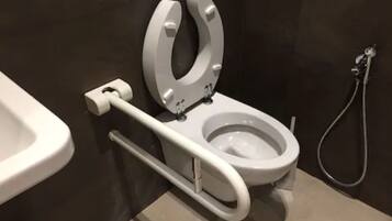 A modern bathroom with a white toilet, a handrail, and a shower area.