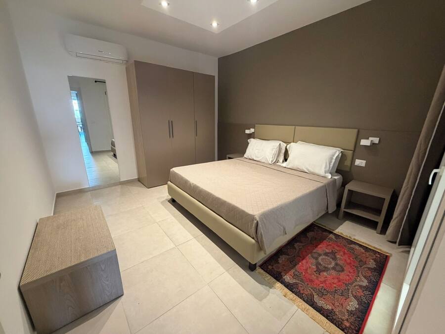 Um quarto moderno com uma cama grande, mesas de cabeceira, um banco e um tapete estampado.