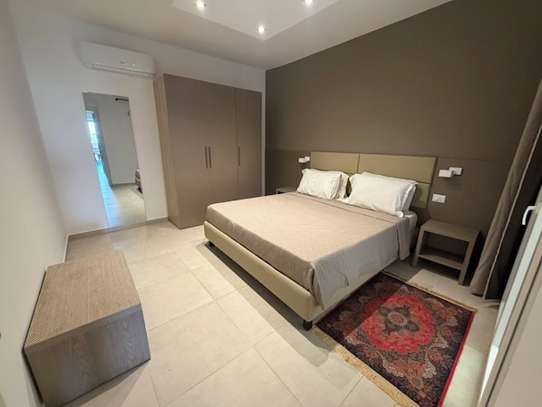A modern bedroom with a large bed, bedside tables, a bench, and a patterned rug.