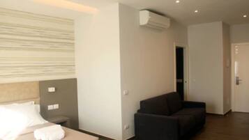 A modern hotel room with a bed, a dark sofa, and an air conditioning unit.
