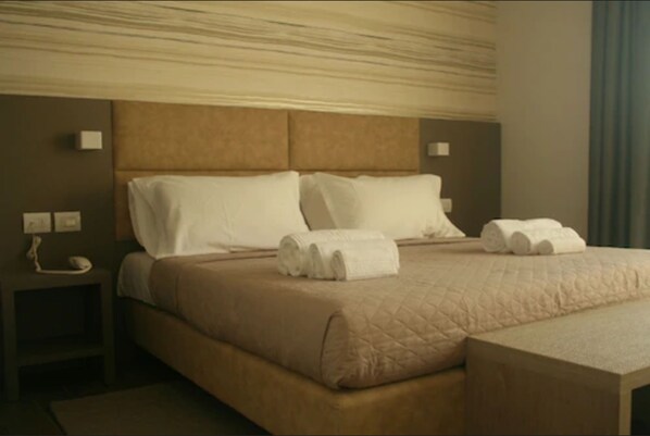 A hotel room with a large bed, a nightstand with a phone, and a headboard with a textured design. - International Hotel Dakar (Dakar)