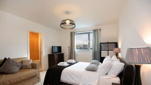 A hotel room with a bed, a sofa, a TV, a lamp, and a window with curtains. - Waterfront Penthouse (Edinburgh)