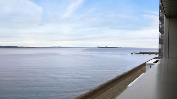 A view from a modern building overlooking a calm body of water with distant landforms. - Waterfront Penthouse (Edinburgh)
