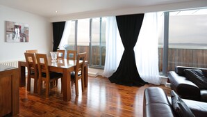 A modern living room with a dining area, large windows, and a view of the outdoors. - Waterfront Penthouse (Edinburgh)