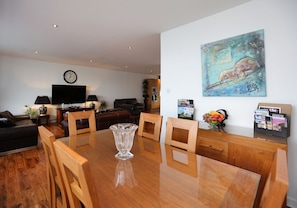 Uma sala de estar moderna com uma mesa de jantar de madeira, cadeiras, uma TV de tela plana, um relógio e um quadro na parede.