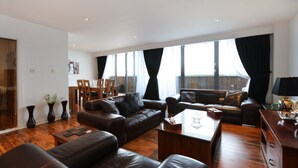 A spacious living room with a leather sofa, a coffee table, and a dining area with chairs and a table. - Waterfront Penthouse (Edinburgh)