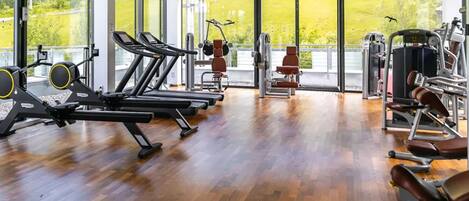 A gym with cardio machines, weight stations, and a large window offering a view of greenery.