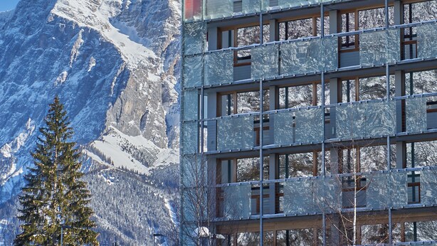 A building with multiple floors, large windows, and a snowy mountain backdrop. - DORMERO BeHo Zugspitze (Biberwier)