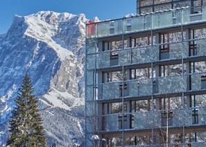 Un edificio de varios pisos, con amplias ventanas y una imponente montaña nevada al fondo.