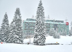 Paisaje nevado con un edificio moderno que tiene fachada de vidrio y un letrero rojo.