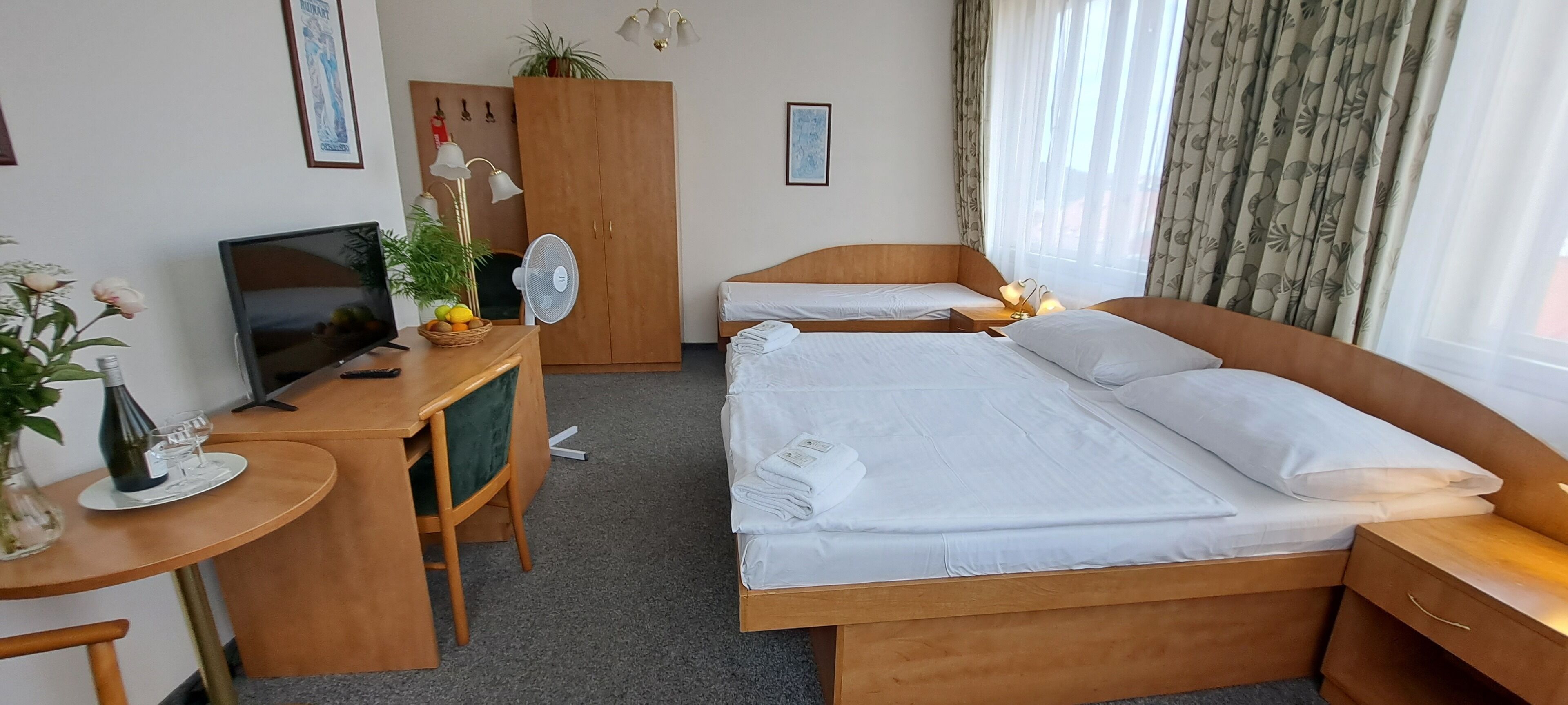 Une chambre d’hôtel comprenant un lit, un bureau avec un ordinateur, une chaise, une armoire et une fenêtre avec des rideaux.