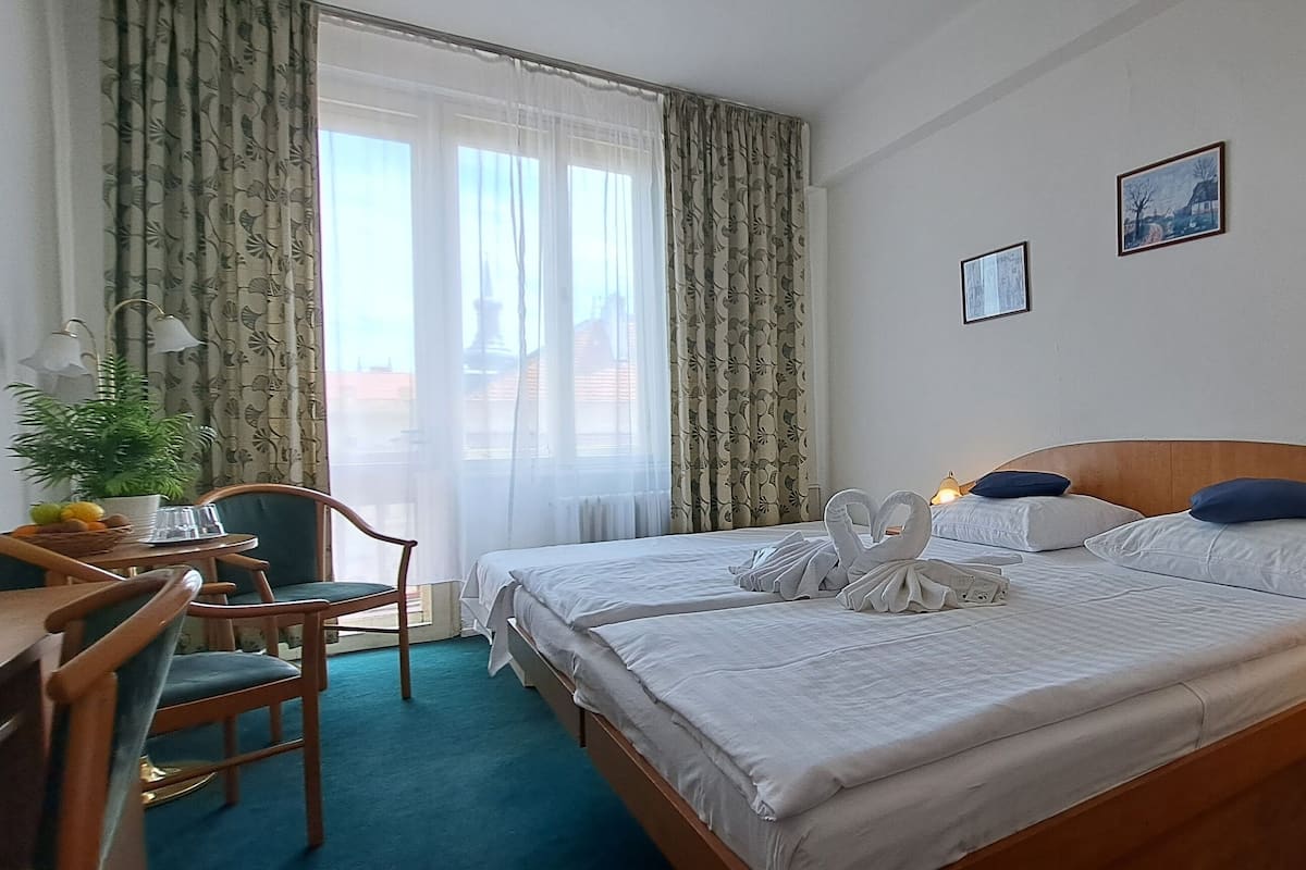 A hotel room with two beds, a desk, chairs, a lamp, and a window with curtains.