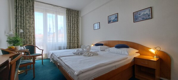 A hotel room with two beds, a desk, chairs, a lamp, and a window with curtains. - Hotel Legie (Prague)