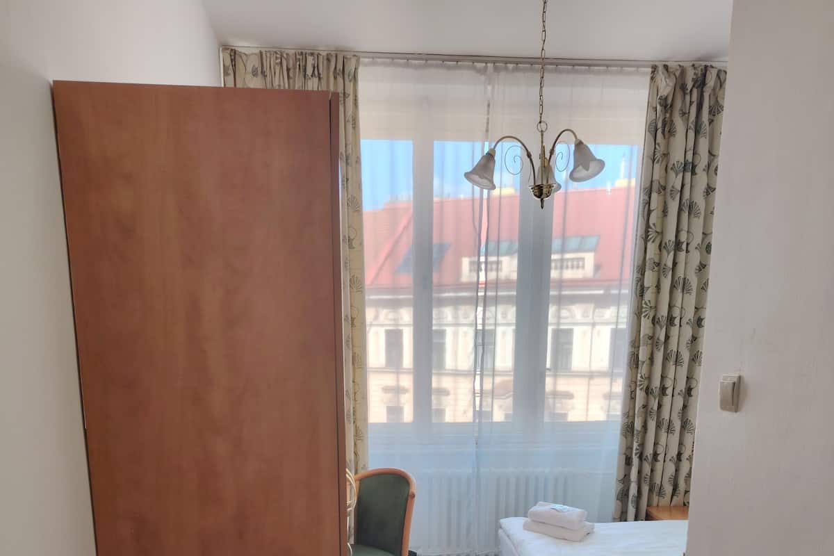 A hotel room with a bed, a chair, a bench, and a window with curtains.