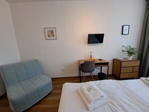 A hotel room with a bed, a desk with a chair, a television, a small table with a plant, and a blue sofa. - Hotel Legie (Prague)