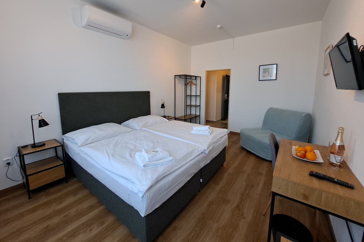 A modern hotel room with a bed, bedside tables, a desk, a chair, and a TV.