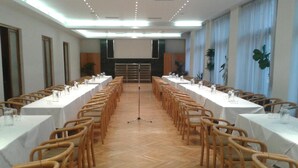 A conference room with long tables and wicker chairs, wooden floors, and large windows with curtains. - Hotel Legie (Prague)