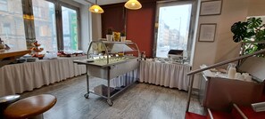 A buffet setup with a variety of food items and a beverage station, situated in a room with large windows and a staircase. - Hotel Legie (Prague)