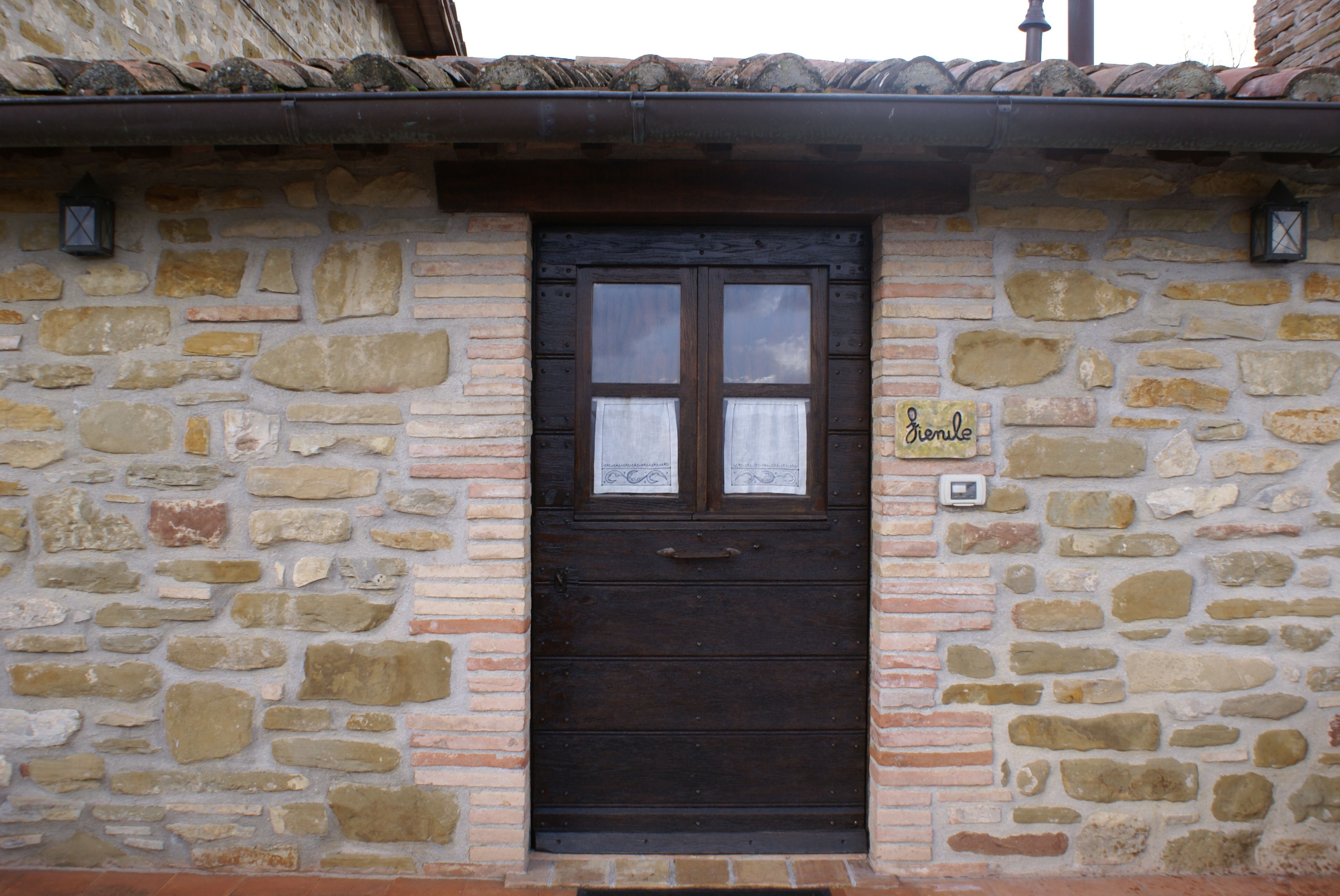 Un edificio de piedra con una puerta de madera oscura, un pequeño cartel sobre la puerta y un farol en la pared.