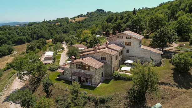 Un bâtiment en pierre doté d’une cour intérieure, entouré d’une végétation luxuriante et de collines.