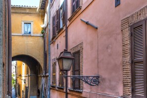 A narrow alleyway with a street lamp and a building with a pink facade and wooden shutters.