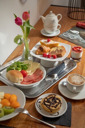 A breakfast table with a variety of food items, including pastries, fruits, and a teapot.