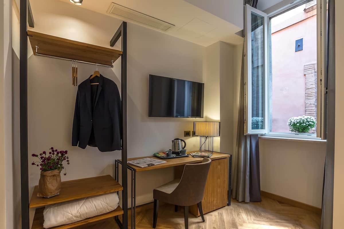 A compact hotel room with a bed, a desk with a chair, a TV mounted on the wall, and a window with curtains.
