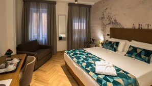 Une chambre d’hôtel avec un grand lit, un canapé, une table à manger avec des produits pour le petit-déjeuner, et une vue sur la ville par la fenêtre.